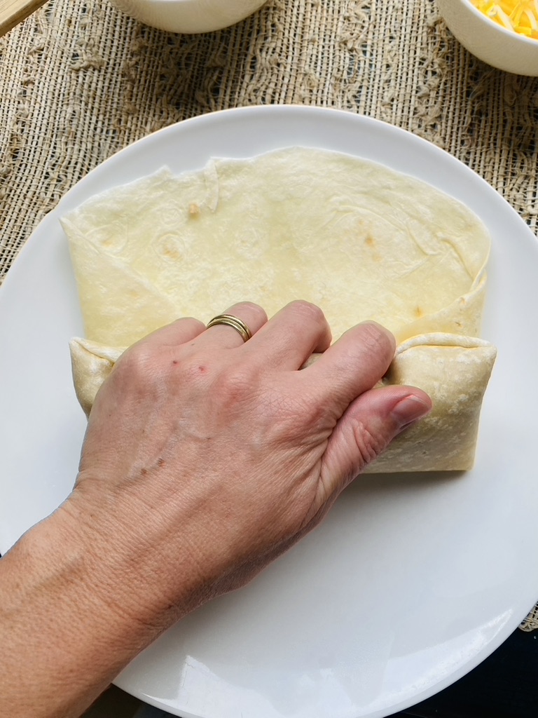 Third step to rolling a burrito, roll the folded tortilla towards end to create packet
