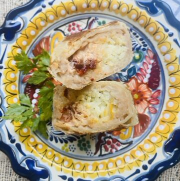 Bean, cheese, rice, and chipotle crema burrito cut in half on a Mexican talavera plate