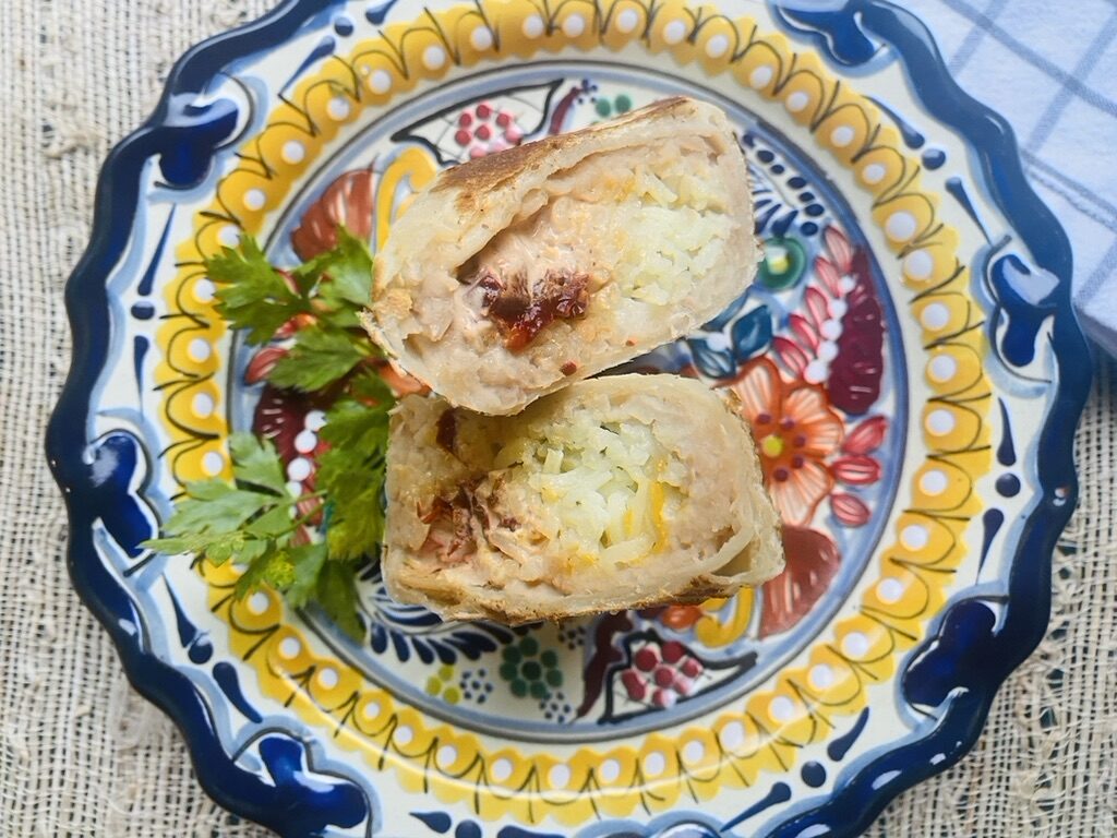 Bean, cheese, rice, and chipotle crema burrito cut in half on a Mexican talavera plate