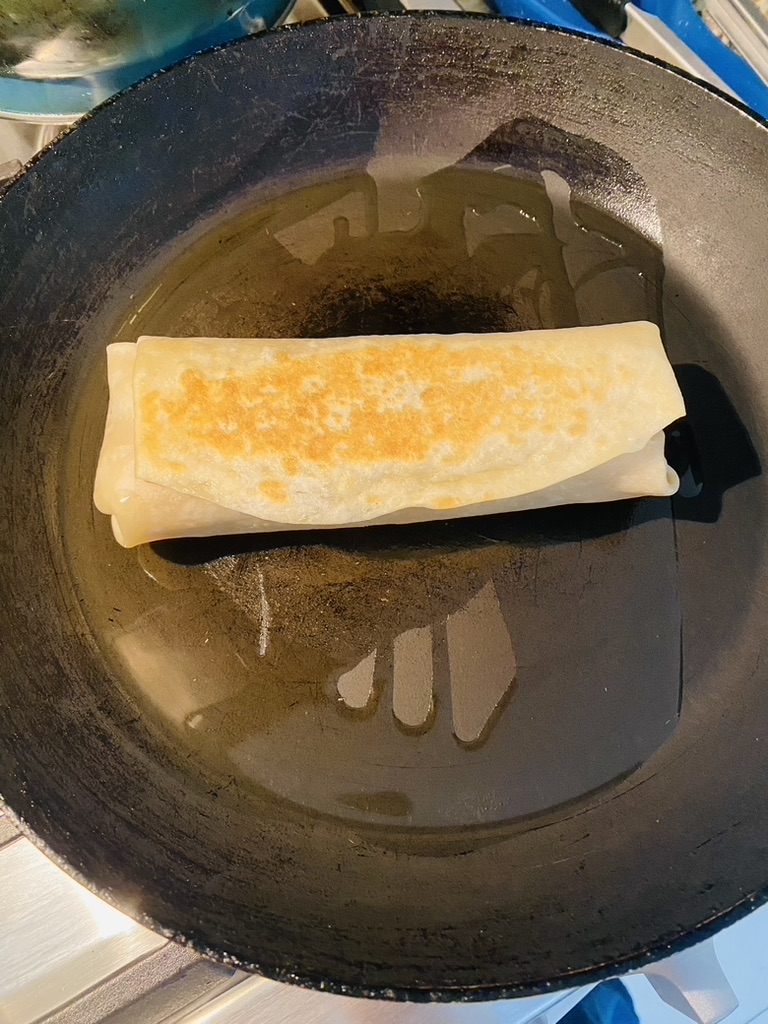 Burrito toasting in a non-stick skillet with hot oil
