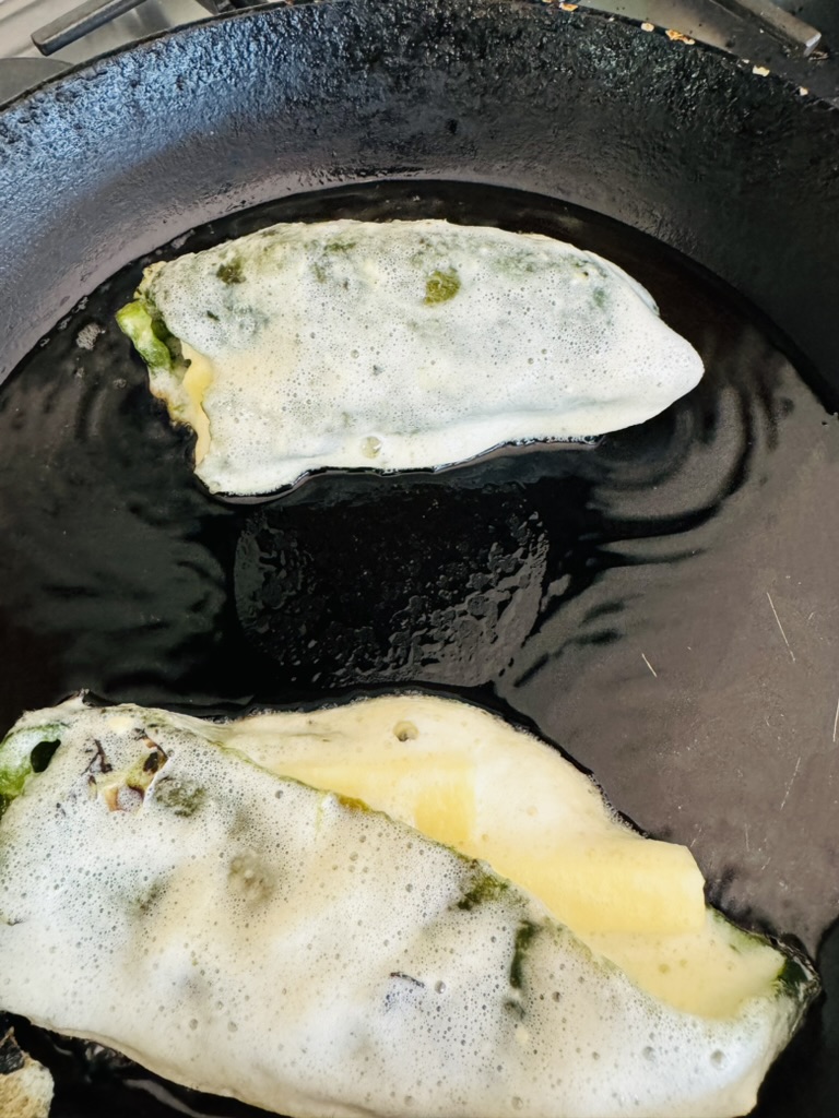 Battered and stuffed poblano peppers frying in pan