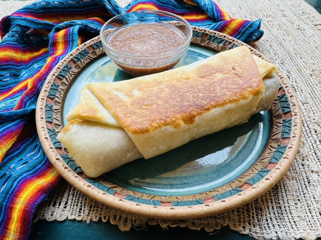 Toasted chile relleno burrito with red salsa on a blue plate