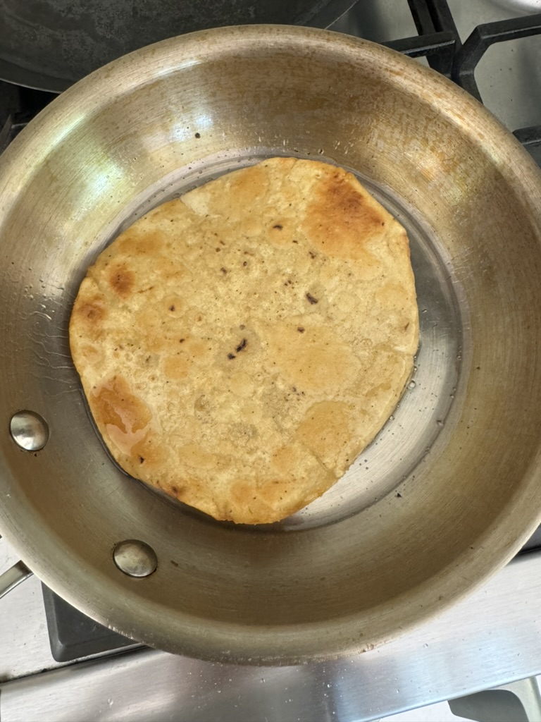 Golden fried corn tortilla in a skillet on the stove. 