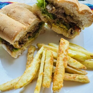 Mexican torta cut in half on a white plate with french fries