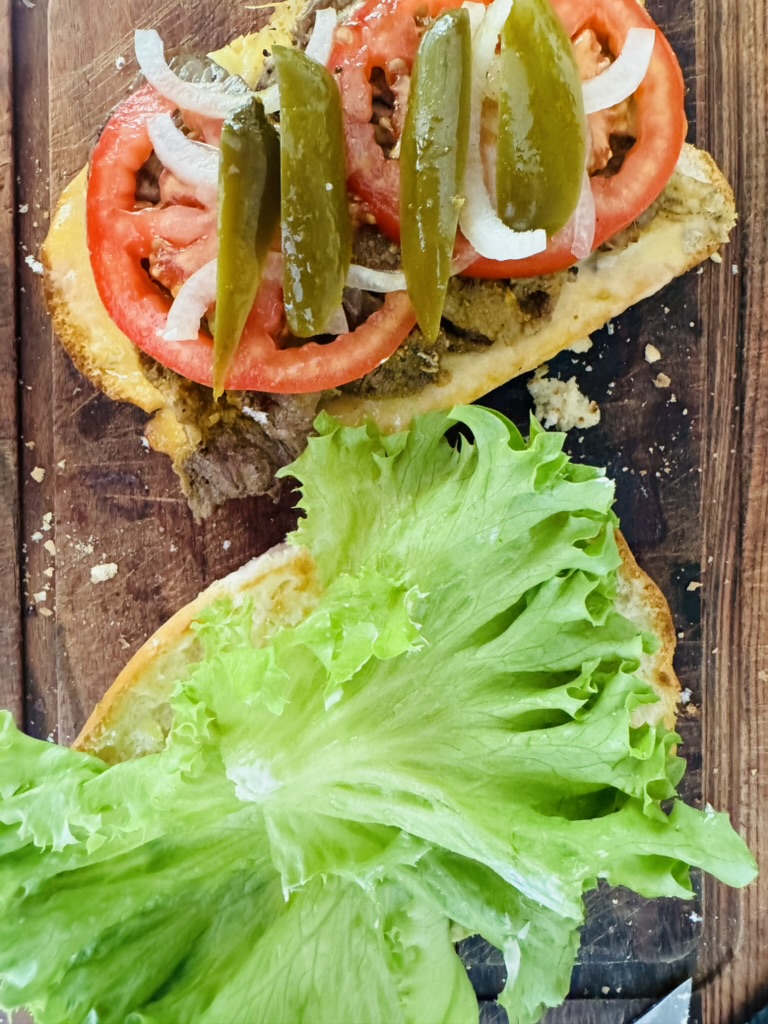 Pickled sliced jalapeños on top of tomatoes, onions, refried beans, and cheese. Other half of torta with avocado, lettuce and mayonnaise