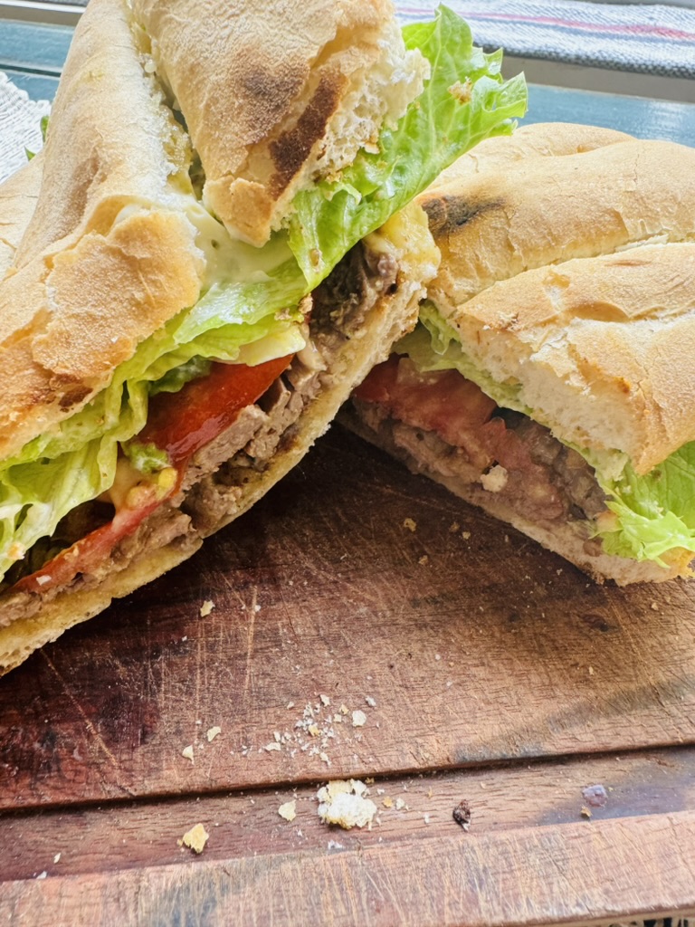 Mexican torta with grilled steak, lettuce, tomatoes, onions, beans, cheese and avocado on a crusty bread, sliced in half