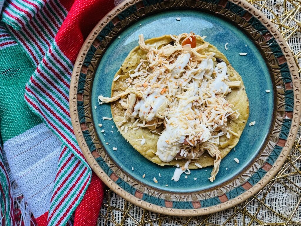Pollo a la mexicana served over a tostada, drizzled with Mexican cream and shredded white Mexican cheese on a blue plate