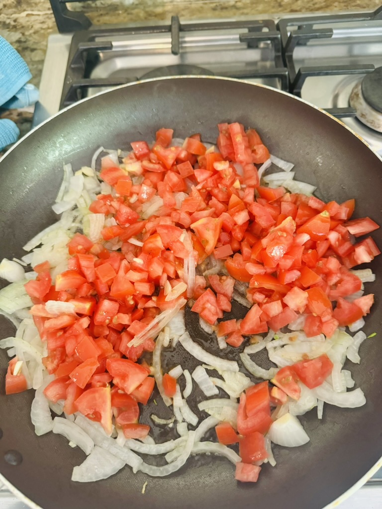 Sliced onions and diced tomatoes frying in a non-stick skillet