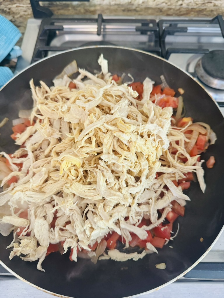 Shredded chicken, sliced onions, and diced tomatoes cooking in a non-stick skillet