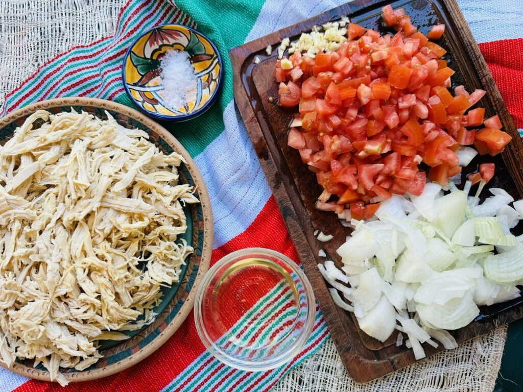 Pollo a la mexicana ingredients. Shredded chicken, diced tomatoes, sliced onions, chopped garlic, salt, and oil 