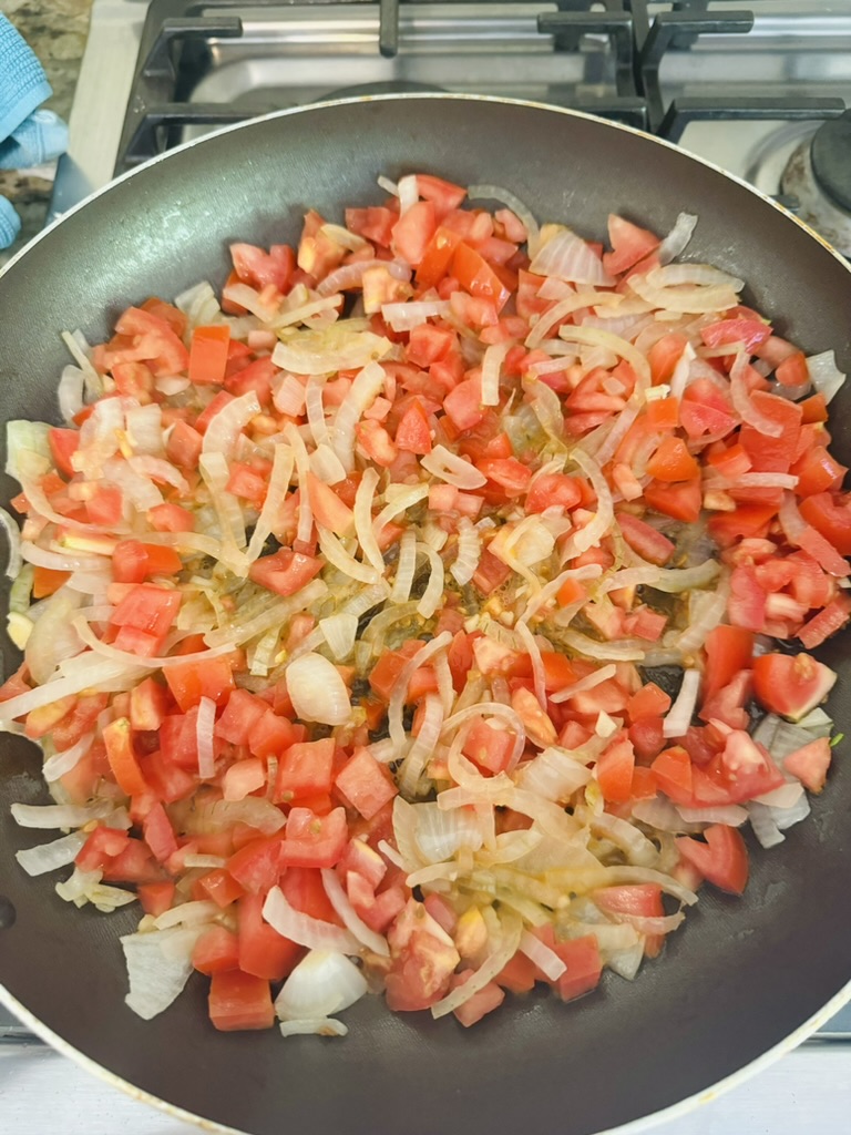 Sliced onions and diced tomatoes cooking in a non-stick skillet