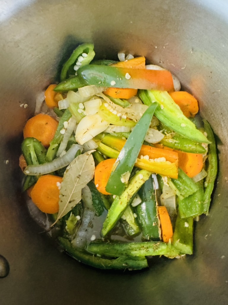 Sliced jalapeño, onions, carrots, and dried herbs cooking in a metal pot