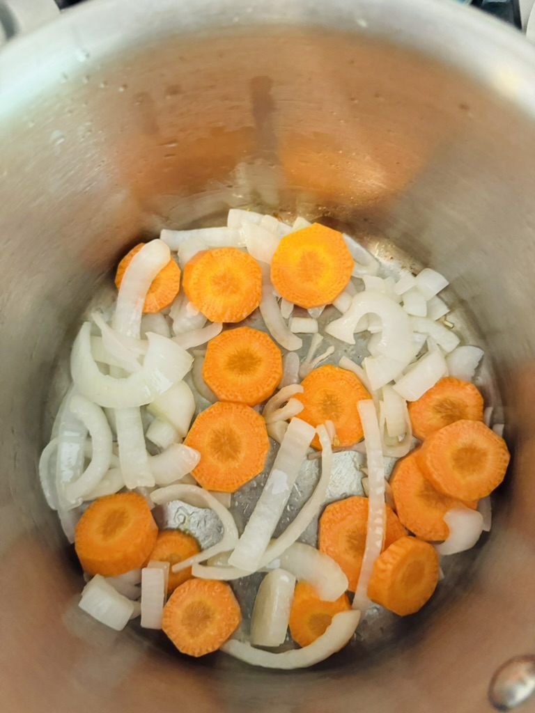 Sliced onions and carrots cooking in a metal pot