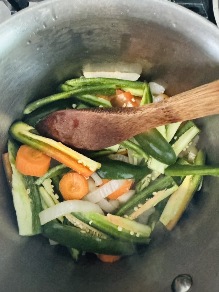 Sliced jalapeños, onions, and carrots cooking in a metal pot