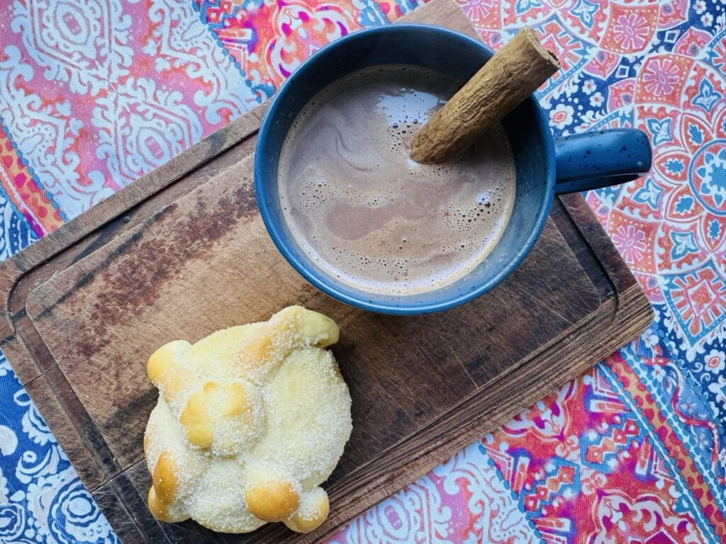 Cup of Mexican hot chocolate in a blue mug with a pan de muerto.