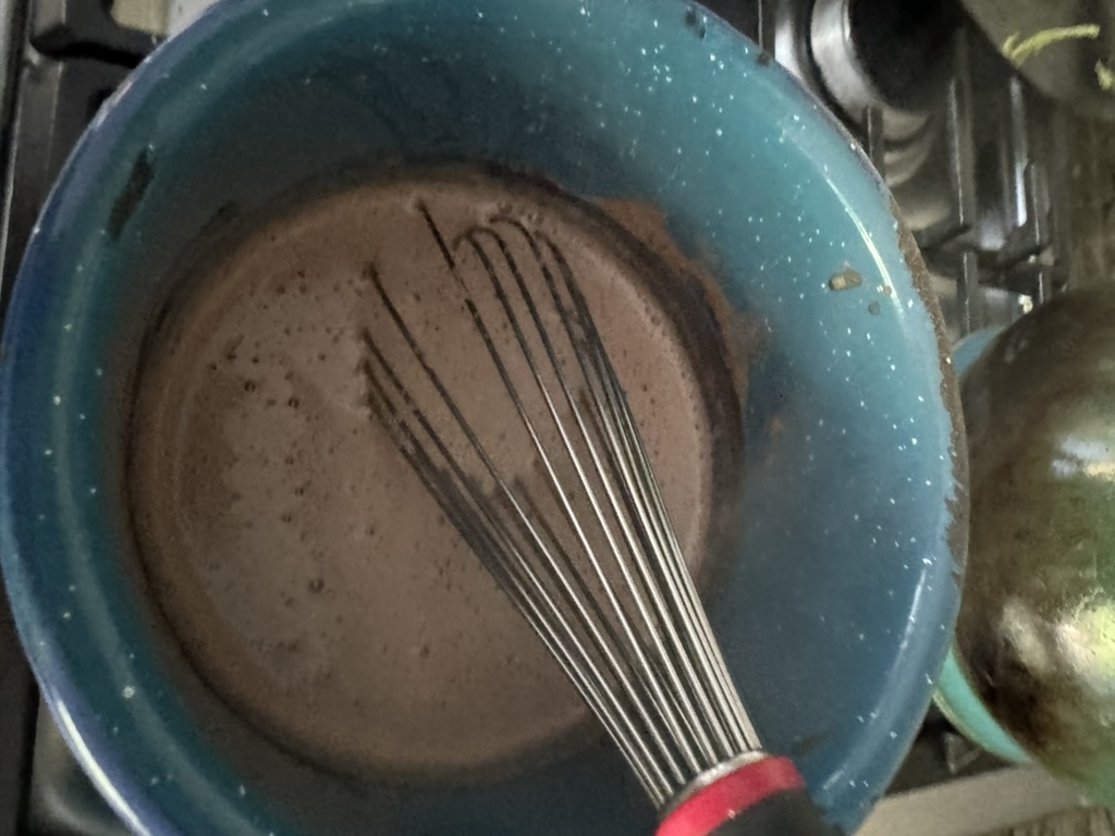 Hot chocolate ingredients in a blue pot with a whisk