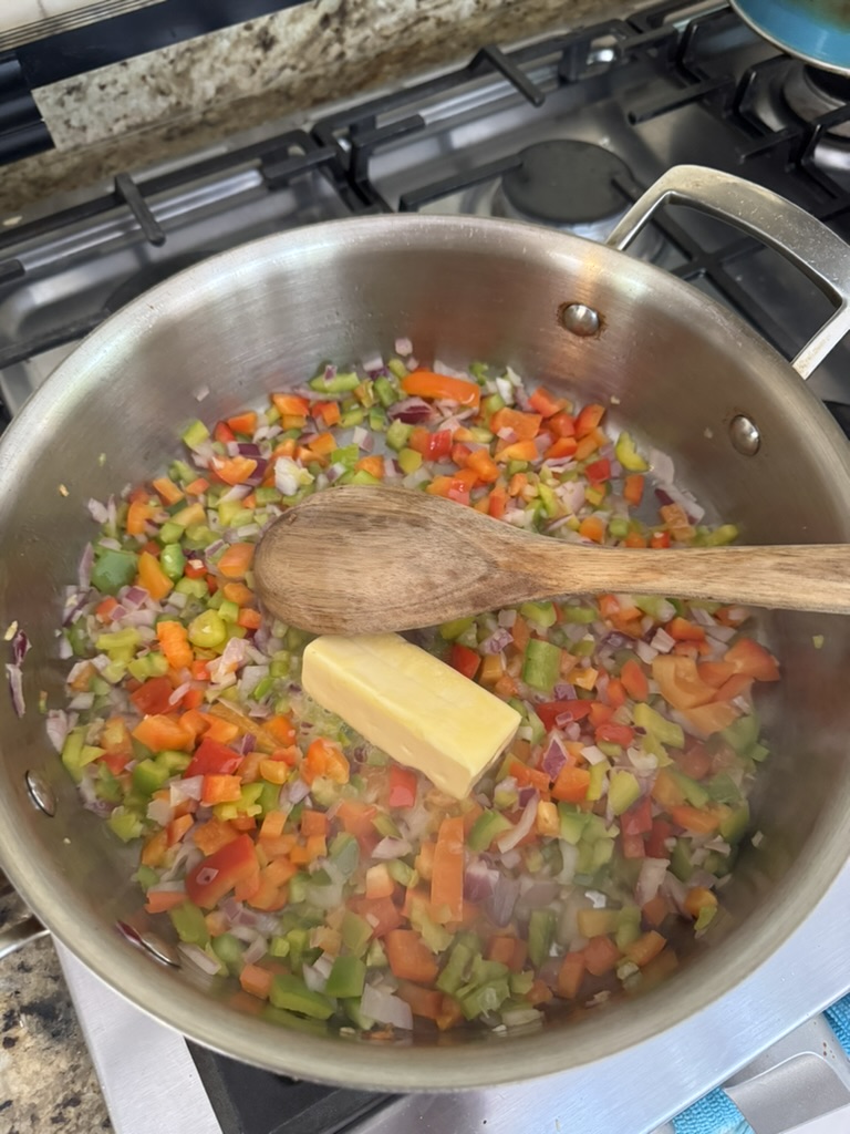 Butter melting in a stainless steel pan with diced onions and bell peppers