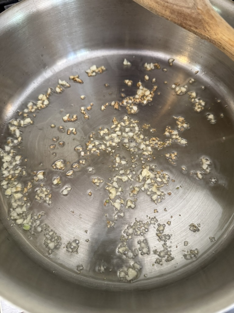 Chopped garlic frying in olive oil in a stainless steel pan