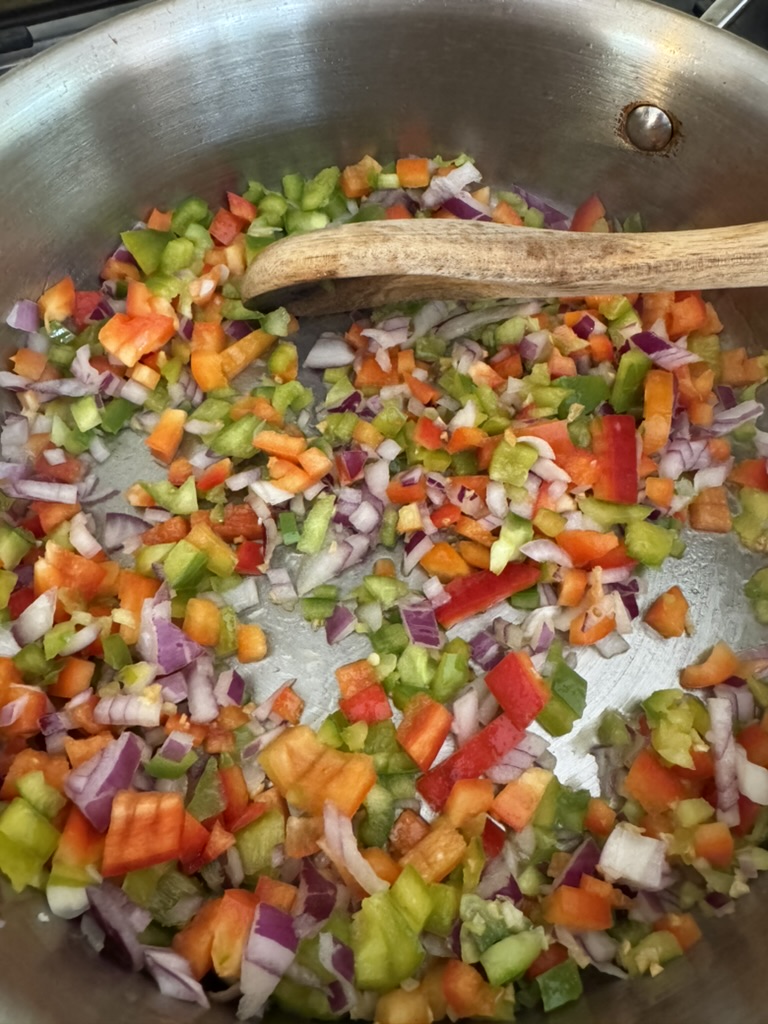 Diced red onion, red pepper, and green pepper frying in olive oil in a stainless steel pan