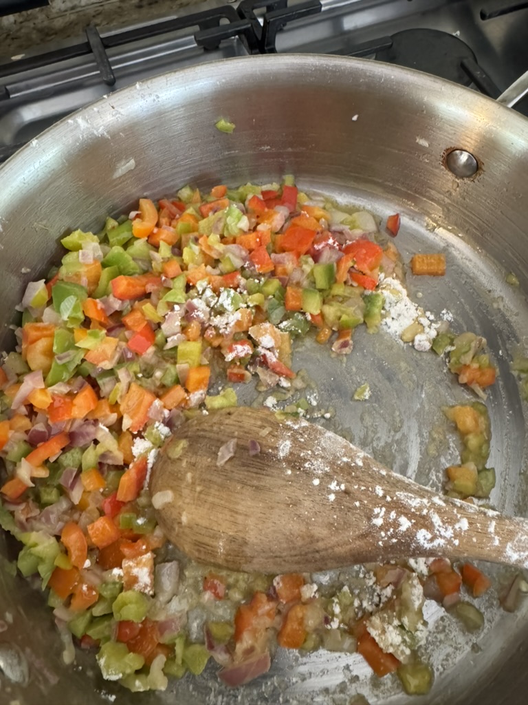 Diced onions and bell peppers sprinkled with a bit of flour in a stainless steel pan