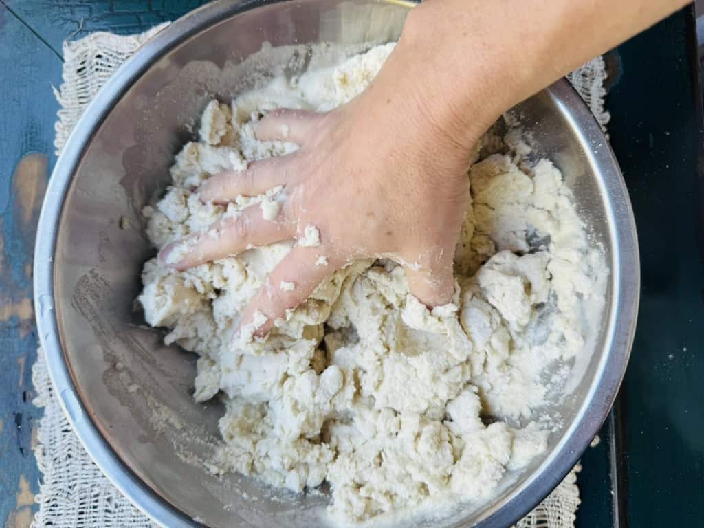 Masa harina and water in a bowl being mixed by hand