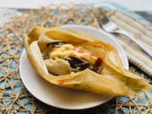 Vegan corn husk tamal with chile strips and cheese on a white plate